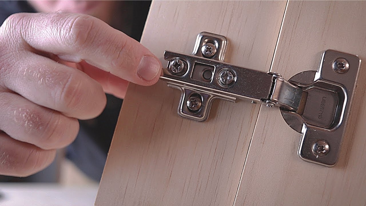 A hand fitting a metal hinge to a light oak-grain door panel