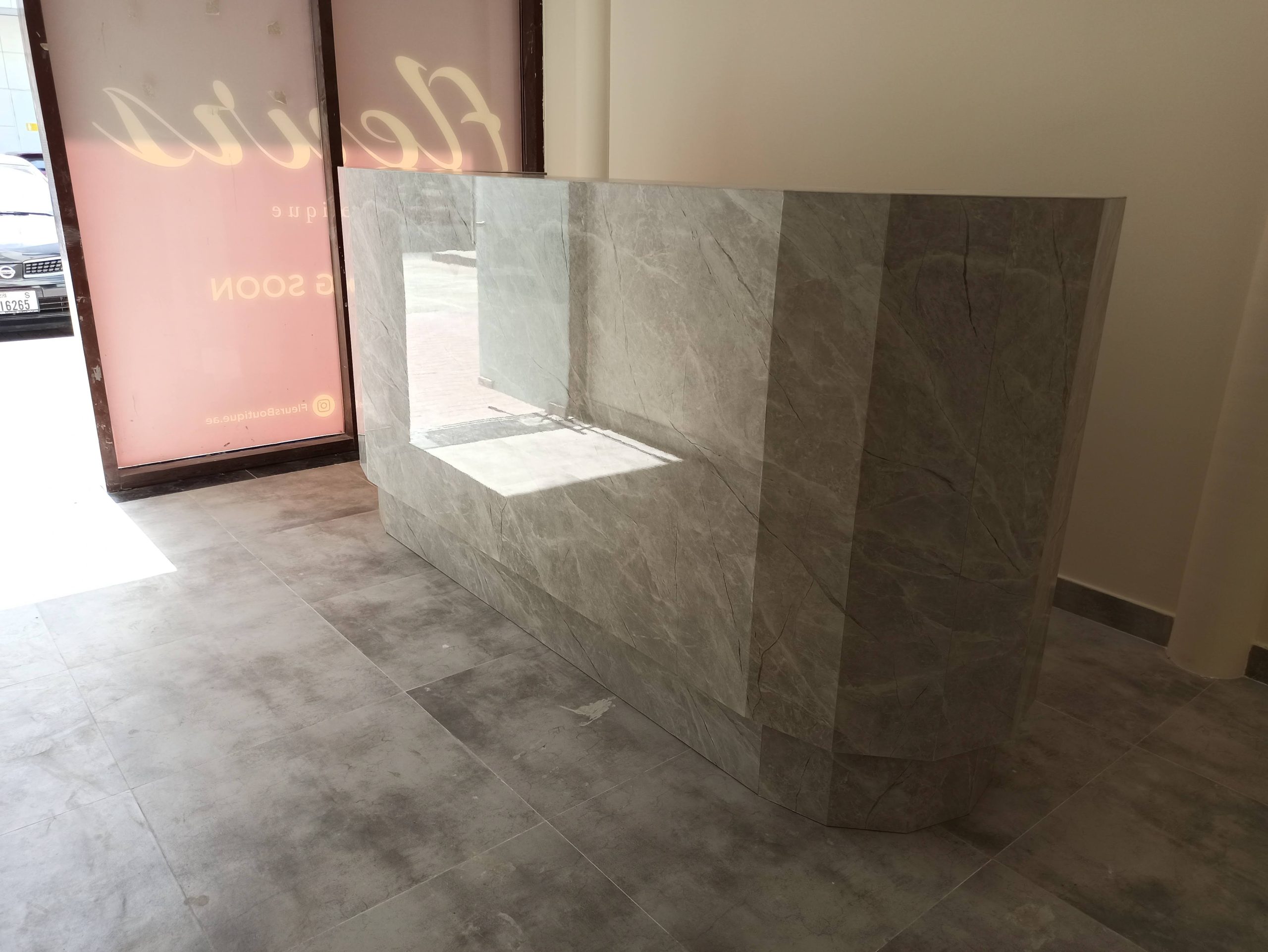Grey veined stone-clad reception counter with a recessed display opening and an angled return, on a grey tiled floor